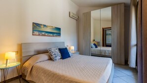 A hotel room with a bed, bedside tables, a painting, a mirror, and a view of the sea. - Villa marta, just 100 m from Cala Caterina (villasimius)