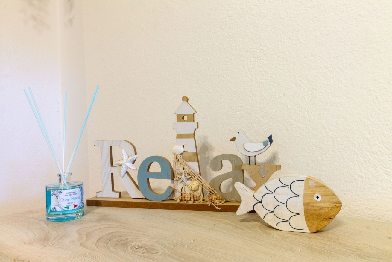 Une étagère en bois ornée d’objets décoratifs, notamment un phare, un oiseau et un poisson, ainsi qu’une bouteille de diffuseur d’ambiance à bâtonnets parfumée à la brise marine.
