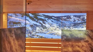 A wooden interior with a large window displaying a snowy mountain landscape. - Hotel Hubertushof (Saalbach-Hinterglemm)
