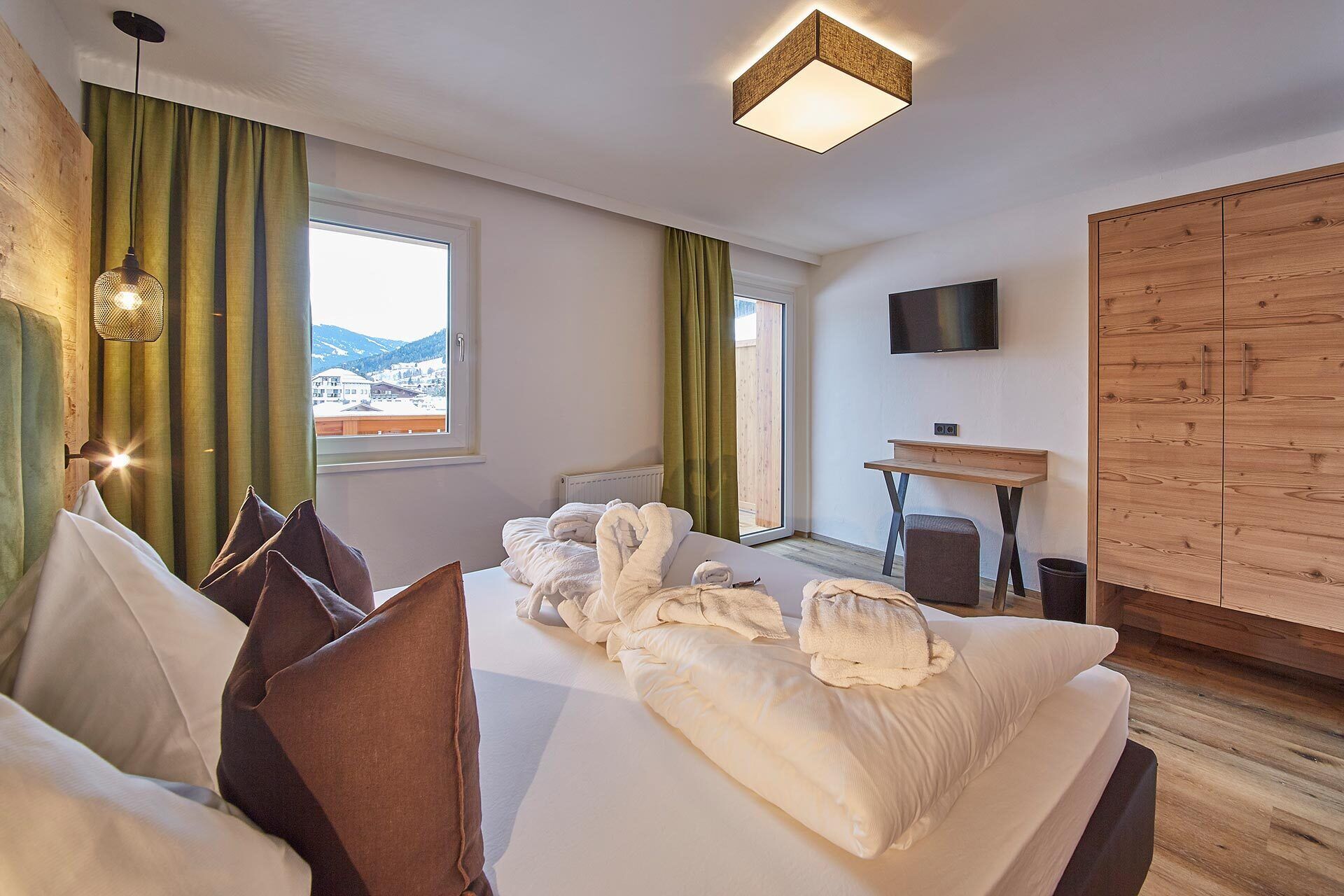 A hotel room with a bed, a desk, a TV, and a view of the outside.