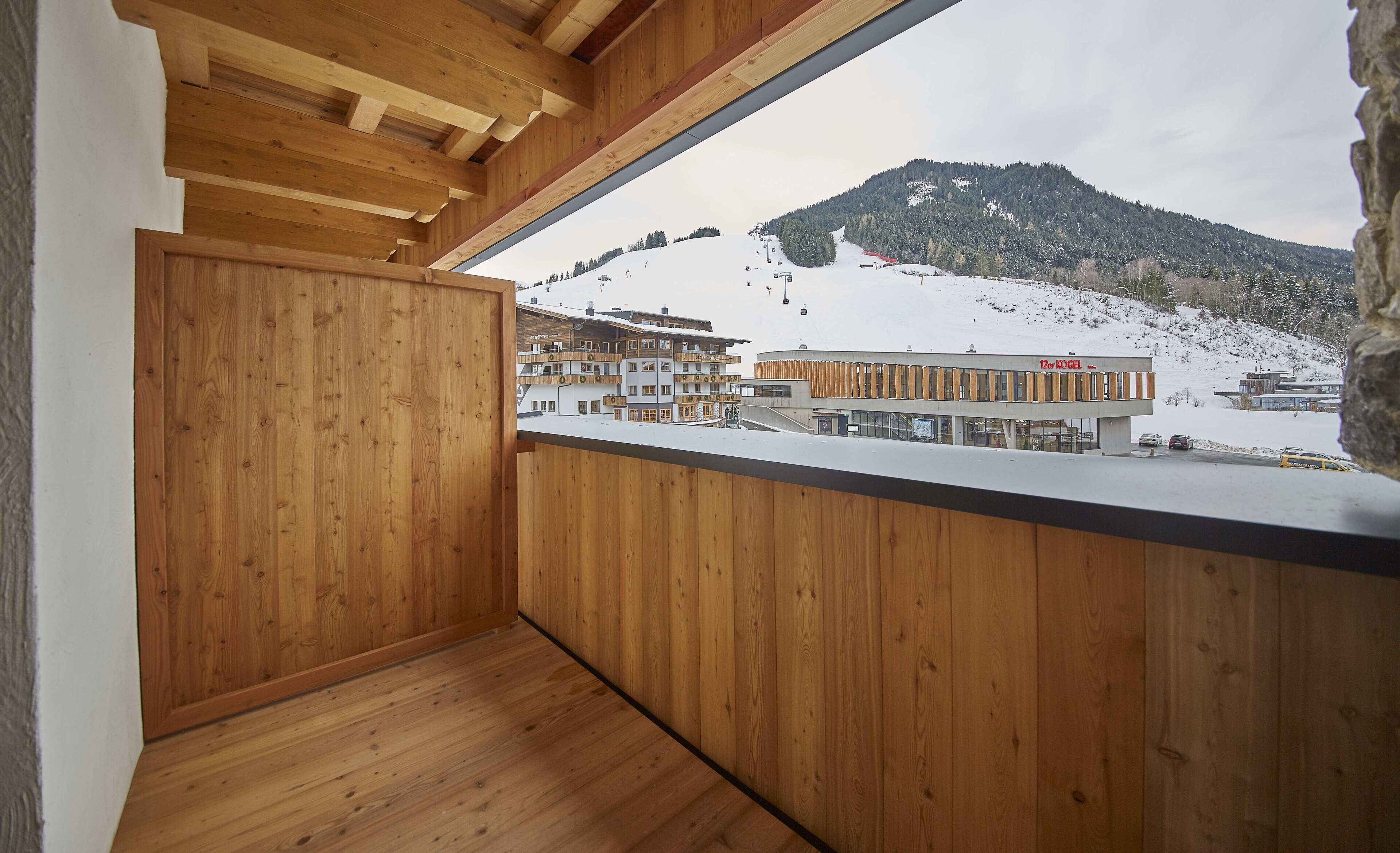 Een houten balkon met uitzicht op een besneeuwde berg en gebouwen.