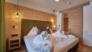 A hotel room with a wooden headboard, a bed with white bedding and towels, and a small wooden side table. - Hotel Hubertushof (Saalbach-Hinterglemm)