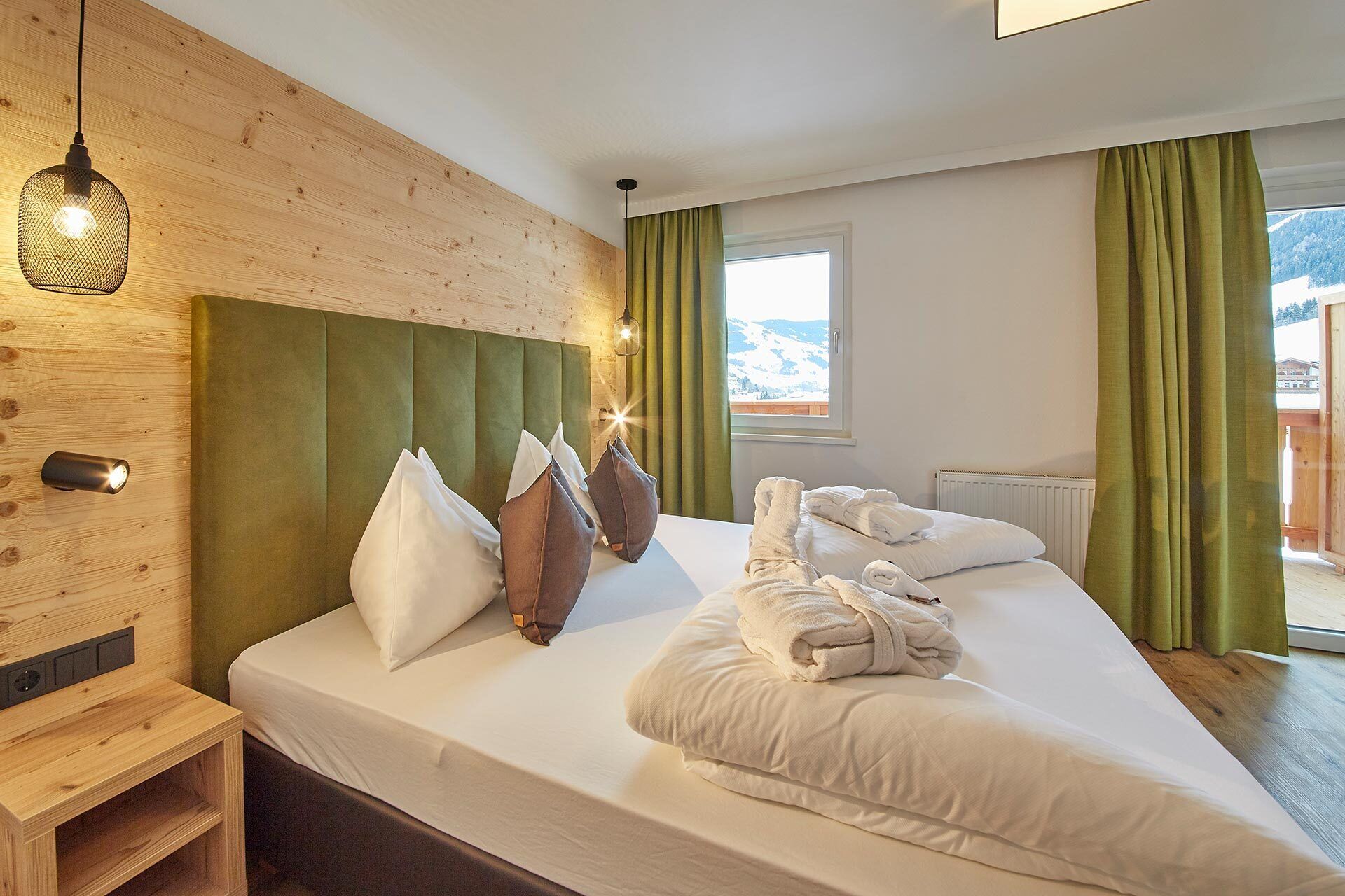 Ein Hotelzimmer mit einem hölzernen Kopfteil, einem großen Bett mit weißen Leinen, mehreren Kissen und Bergblick durch ein Fenster.