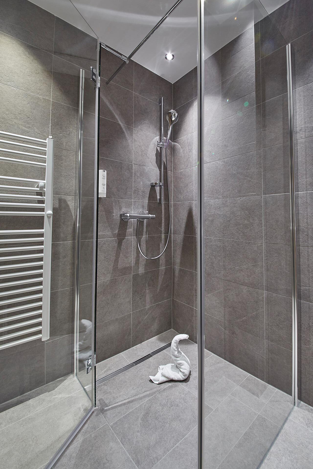 Une douche moderne avec une porte en verre, un pommeau de douche à main et une serviette sur le sol.