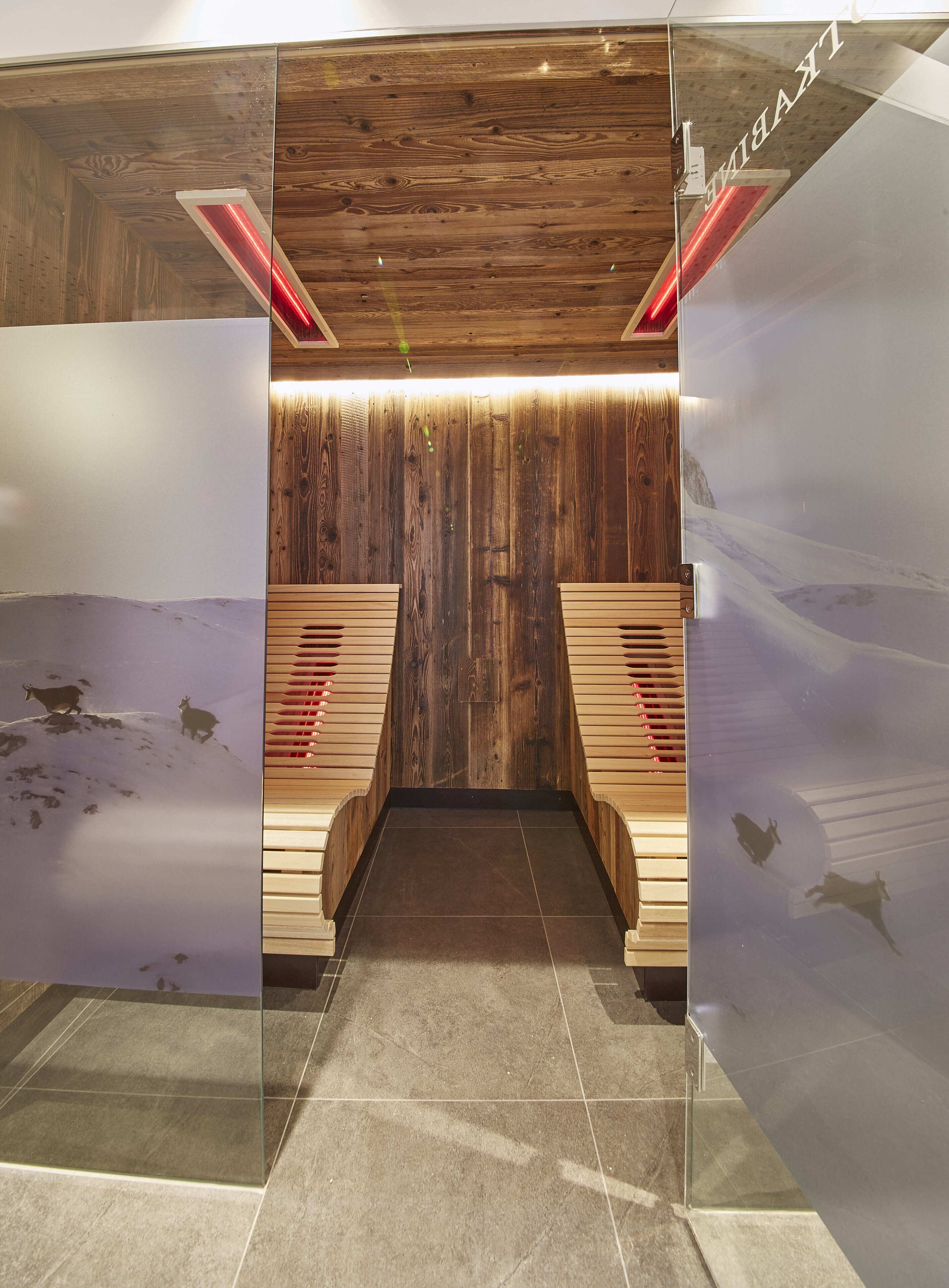 A sauna room with wooden walls and benches, a tiled floor, and a glass partition with a mountain view.