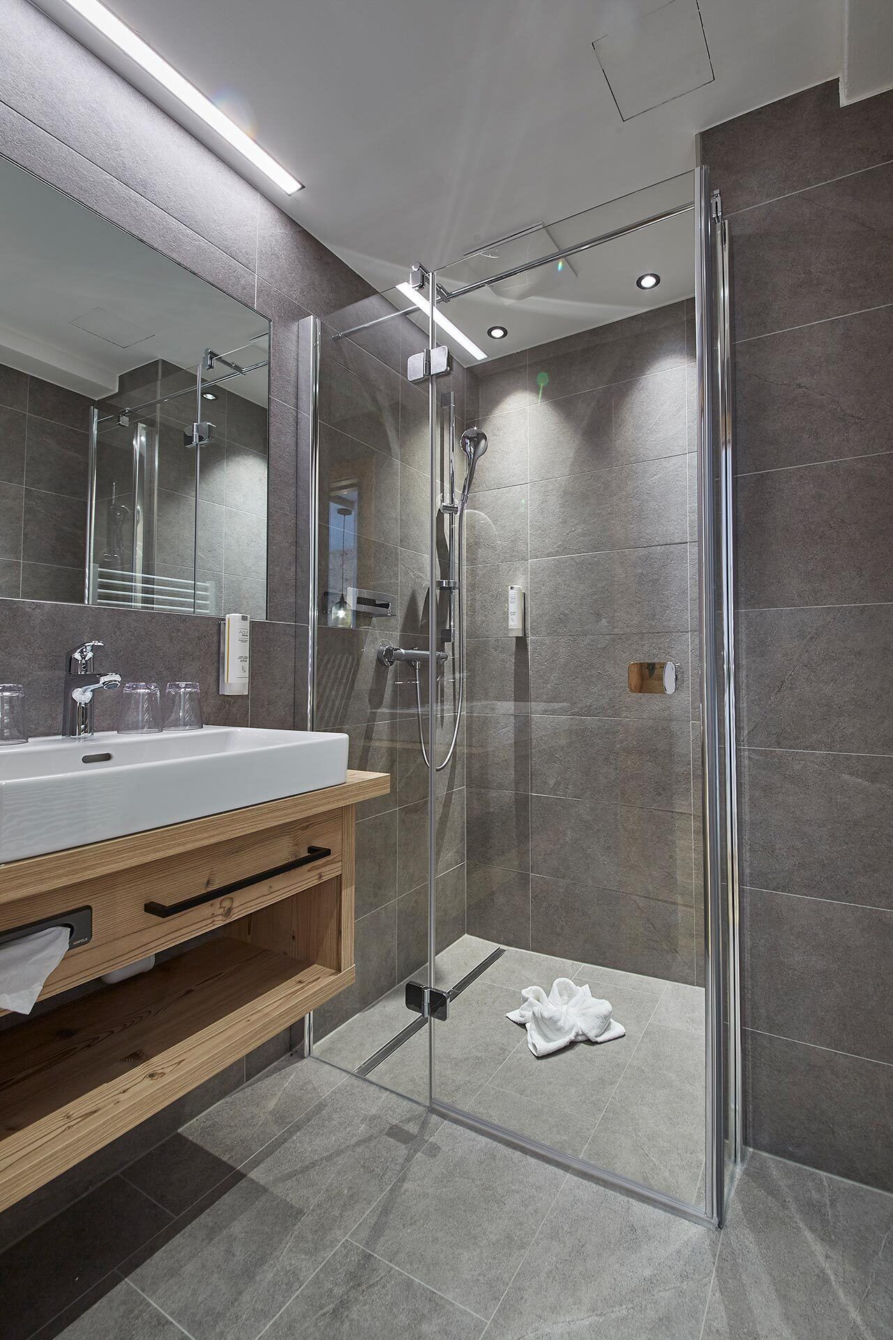 A modern bathroom with a glass-enclosed shower, a wooden vanity, and a large mirror.