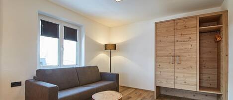 Un salon moderne avec un canapé gris, une table basse ronde en bois, un lampadaire, une armoire aux portes en bois et une fenêtre avec des stores.