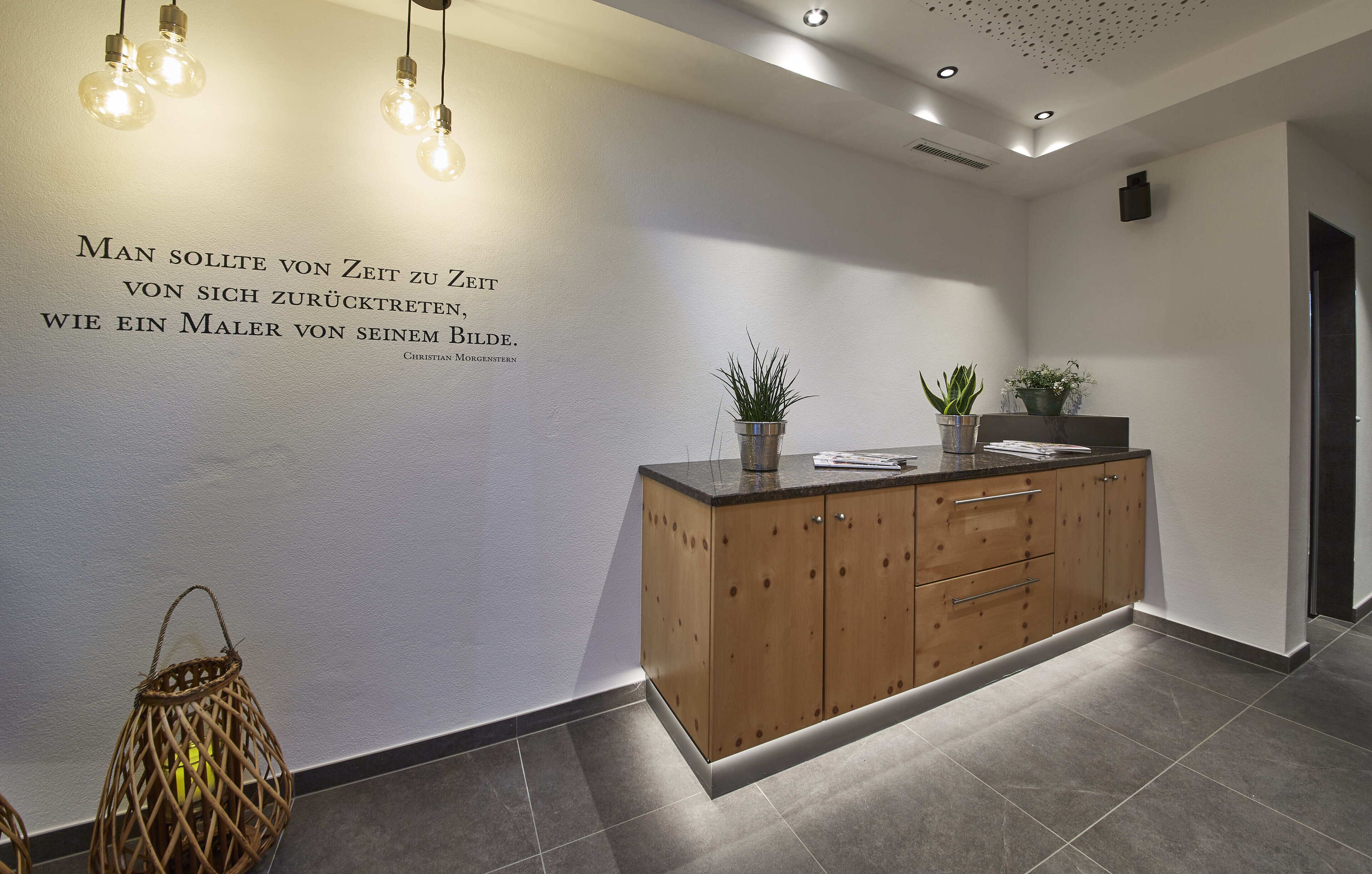 A modern reception area with a wooden cabinet, a wall-mounted quote, and a hanging light fixture.