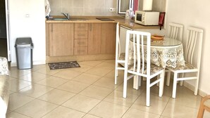 A compact kitchen with wooden cabinets, a sink, and a microwave. There's a dining table with chairs and a small rug on the floor. - minerva 1 bedroom ap (Benalmádena)