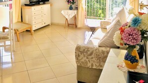 A living room with a television, a small table with a vase of flowers, a sofa, and a balcony with a view of greenery. - minerva 1 bedroom ap (Benalmádena)