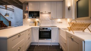 Eine kompakte Küche mit weißen Schränken, einem eingebauten Backofen und einer Arbeitsplatte mit Wasserkocher und Besteck.
