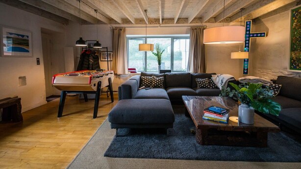 Ein gemütliches Wohnzimmer mit einem Kicker, einer Sofagarnitur und einem Couchtisch mit Büchern und einer Vase.