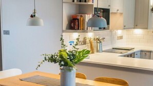 Eine moderne Küche mit weißen Schränken, einem Holztisch mit vier Stühlen und einer hängenden Pendelleuchte.
