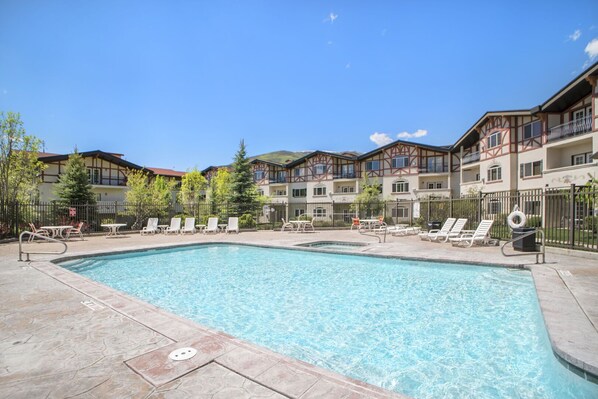 A swimming pool with lounge chairs and a fenced area, surrounded by multi-story buildings with balconies.