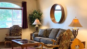 A living room with a sofa, two armchairs, a coffee table, and a round mirror on the wall.