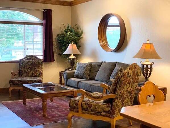 A living room with a sofa, two armchairs, a coffee table, and a round mirror on the wall.