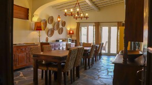 A dining area with a stone floor, wooden furniture, and a chandelier.