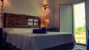 A bedroom with a wooden headboard, a bed with a white bedspread, a blue pillow, a bedside lamp, and a view of the outdoors through a sliding glass door.
