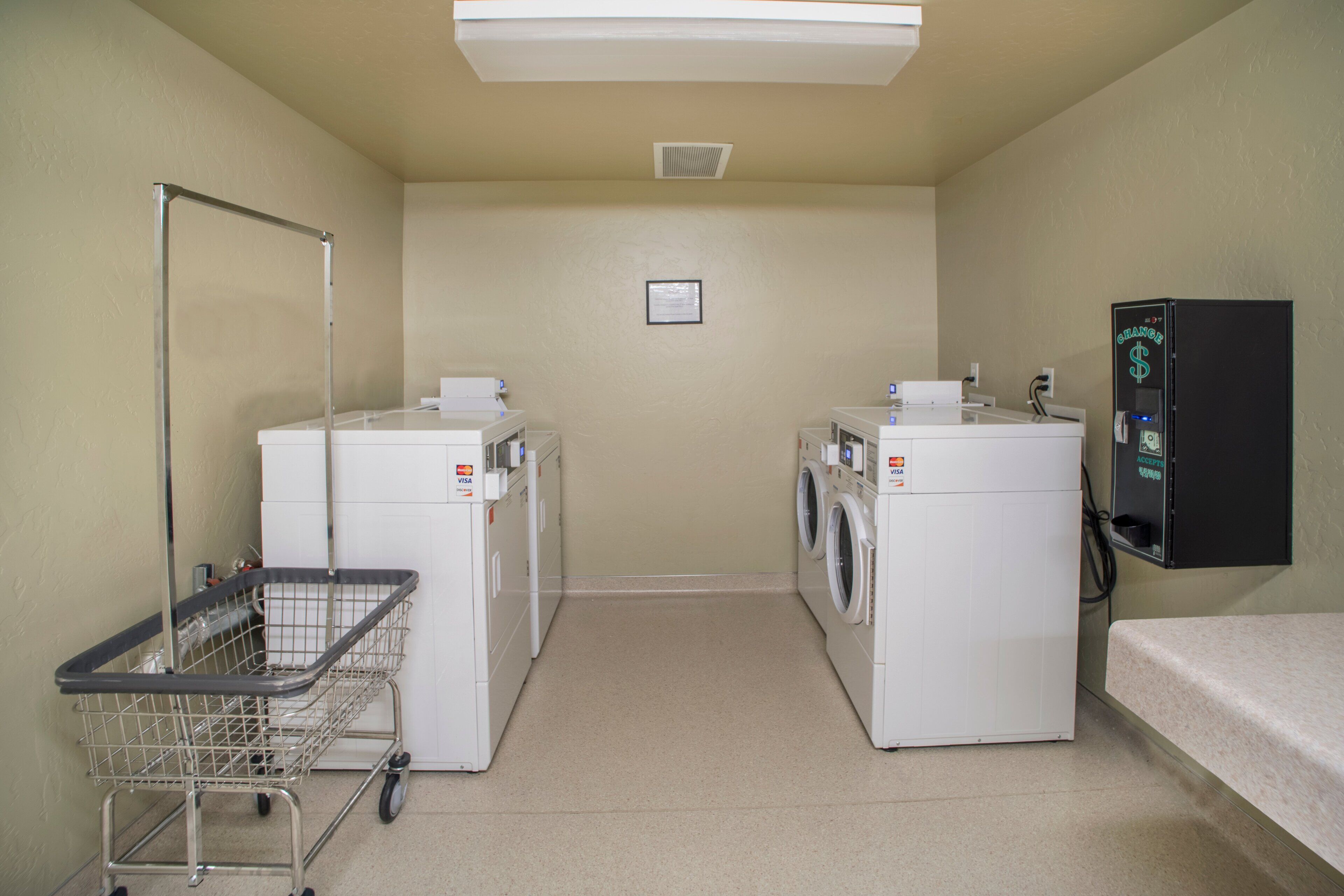 A laundry room with two washing machines, a dryer, a vending machine, and a cart.