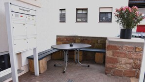 An outdoor seating area with a table and benches, a stone wall, and a flower pot. - Would you like to experience a vacation in the heart of the Palatinate on the German Wine Route? (Deidesheim)