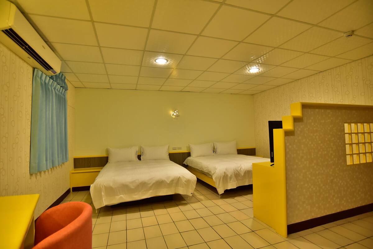 Habitación de hotel con dos camas, una mesita, una silla y un equipo de aire acondicionado.