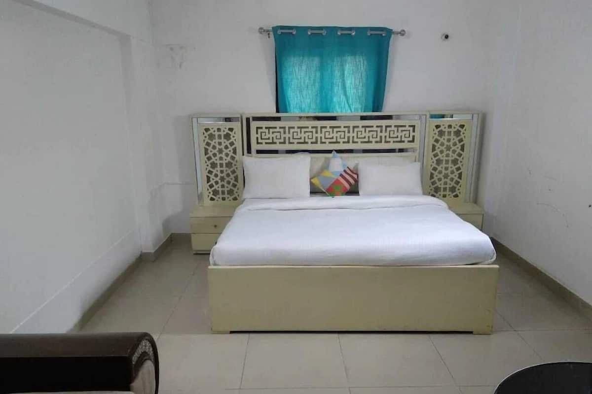A single bed with a white mattress and a decorative headboard, a teal curtain, and a small bedside table with a lamp.