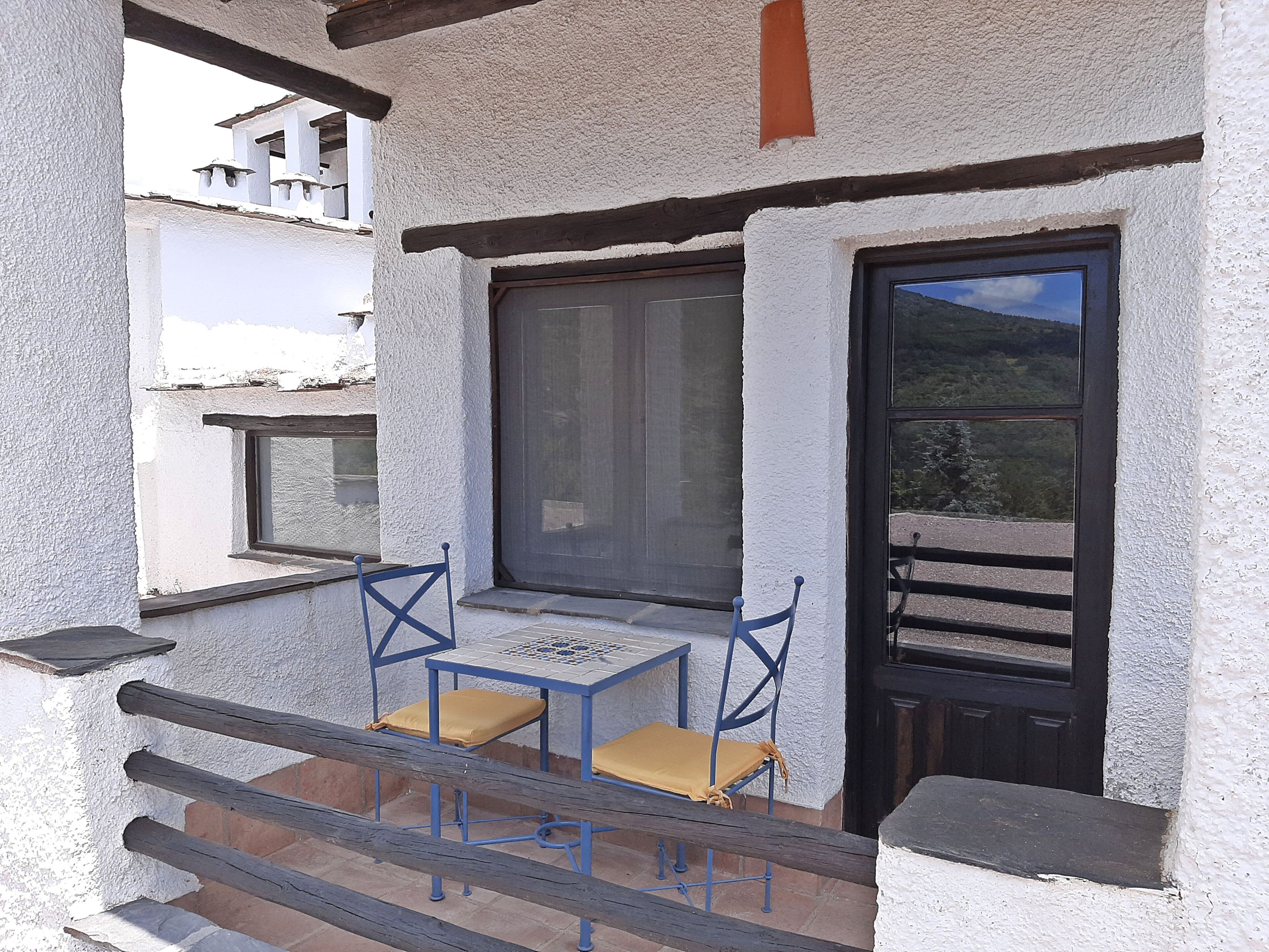 A balcony with a table and two chairs, a door, and a window.