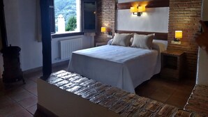 Quarto com cama, duas luminárias de cabeceira, janela com persianas, radiador e parede de tijolos.