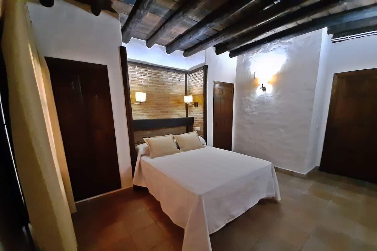 Quarto com cama, porta de madeira, parede de tijolos e luminária fixada na parede.