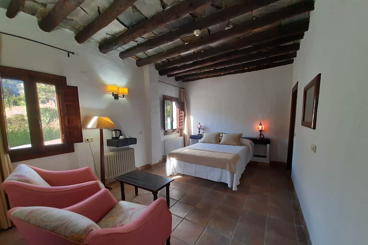 Quarto com cama, abajures, radiador, janela e uma cadeira rosa.