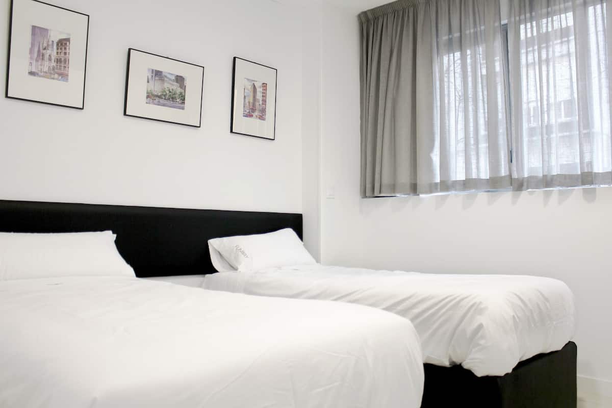 Una habitación de hotel con dos camas, un cabecero negro y tres cuadros enmarcados en la pared.