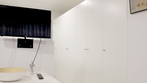 A modern room with a flat-screen TV mounted on the wall, a white table with a bowl and a remote, and white cabinets. - Apartamentos Funway Hostel (Madrid)