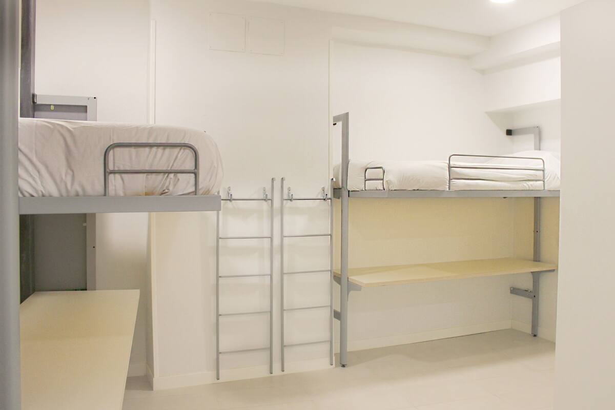 Habitación con literas, un escritorio y una estantería.