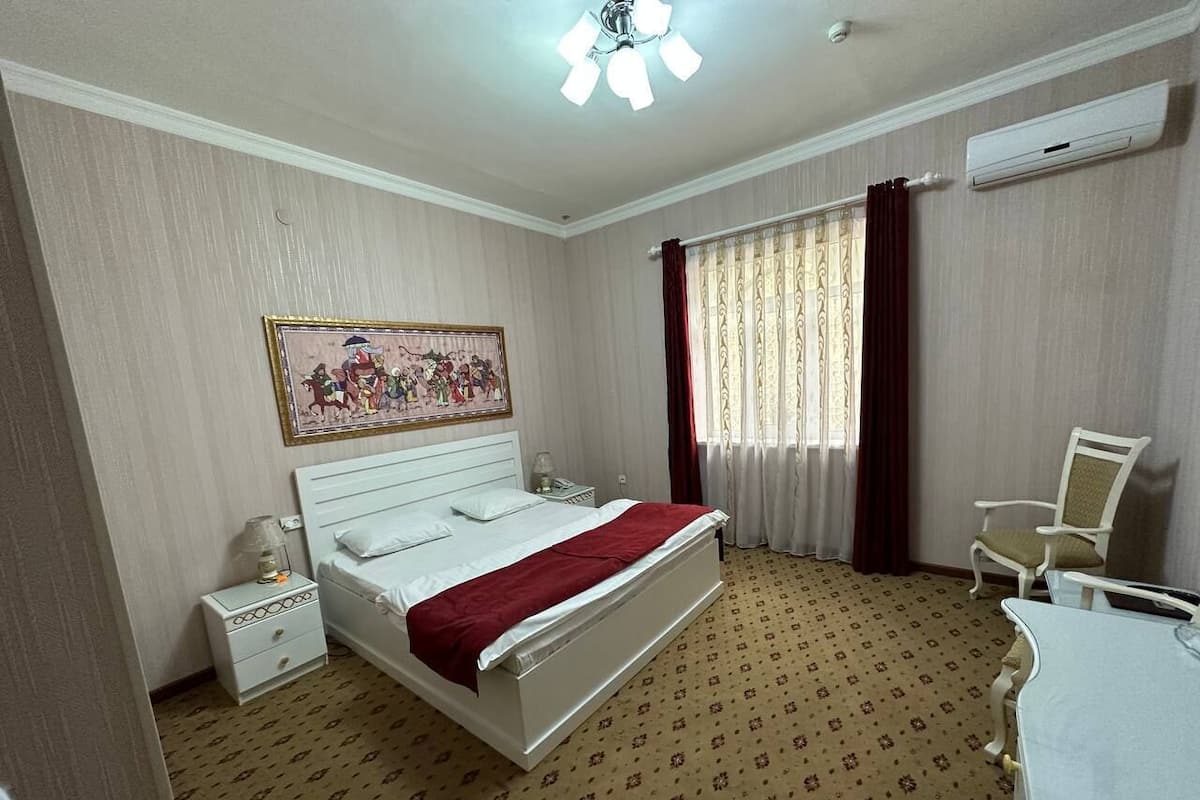 A hotel room with a bed, a nightstand, a chair, a desk, and a window with curtains.