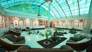 A spacious lobby with a high glass ceiling, multiple seating areas, and decorative plants. - Reikartz Modarixon Bukhara (Bukhara)