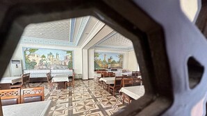 A dining area with tables and chairs, a patterned floor, and a mural on the wall. - Reikartz Modarixon Bukhara (Bukhara)