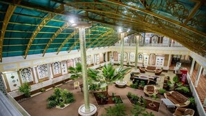 A spacious atrium with a high ceiling, multiple seating areas, and a variety of plants. - Reikartz Modarixon Bukhara (Bukhara)