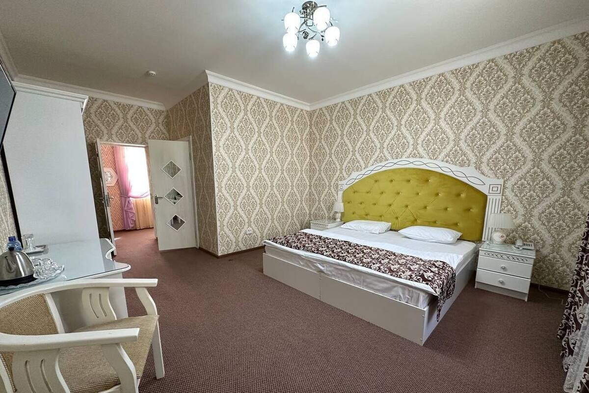 A bedroom with a bed, bedside table, chair, and a desk with a lamp.