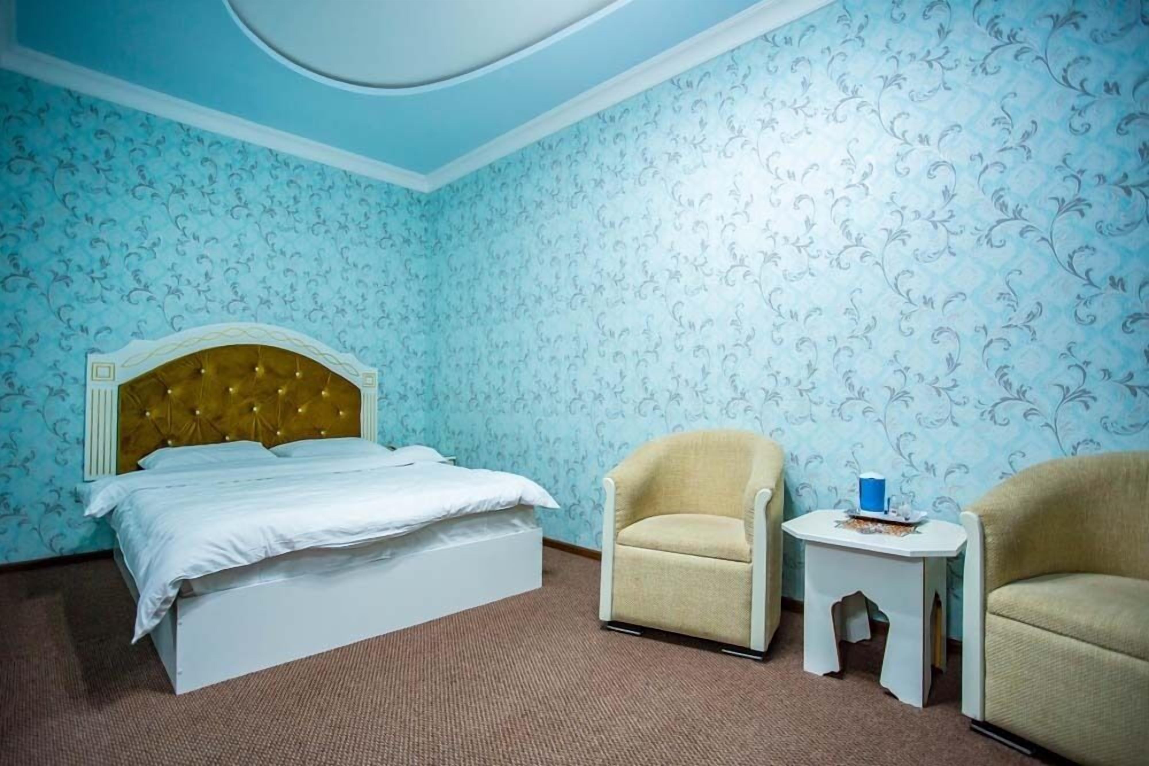 Een hotelkamer met een bed, twee fauteuils, een tafeltje en behang met een patroon.