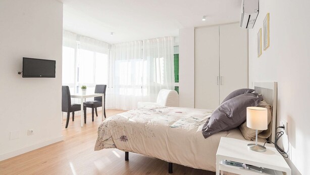 A bedroom with a bed, bedside table, lamp, and a TV mounted on the wall. - Beautiful Studio Near the Beach (Malaga)