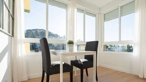 A room with a dining table and two chairs, large windows, and a view of a cityscape. - Beautiful Studio Near the Beach (Malaga)