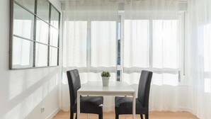 Une pièce avec une table et deux chaises, une plante en pot posée sur la table et une grande fenêtre ornée de rideaux légers.