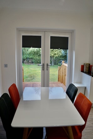 Enjoy meals in the room's dining area with a table and four chairs, offering a view of the outdoor deck and grassy yard.
