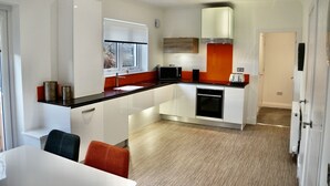 Una cocina moderna con armarios blancos, encimera negra y pared de acento roja. Hay un ventanal sobre el fregadero y un microondas en la encimera.