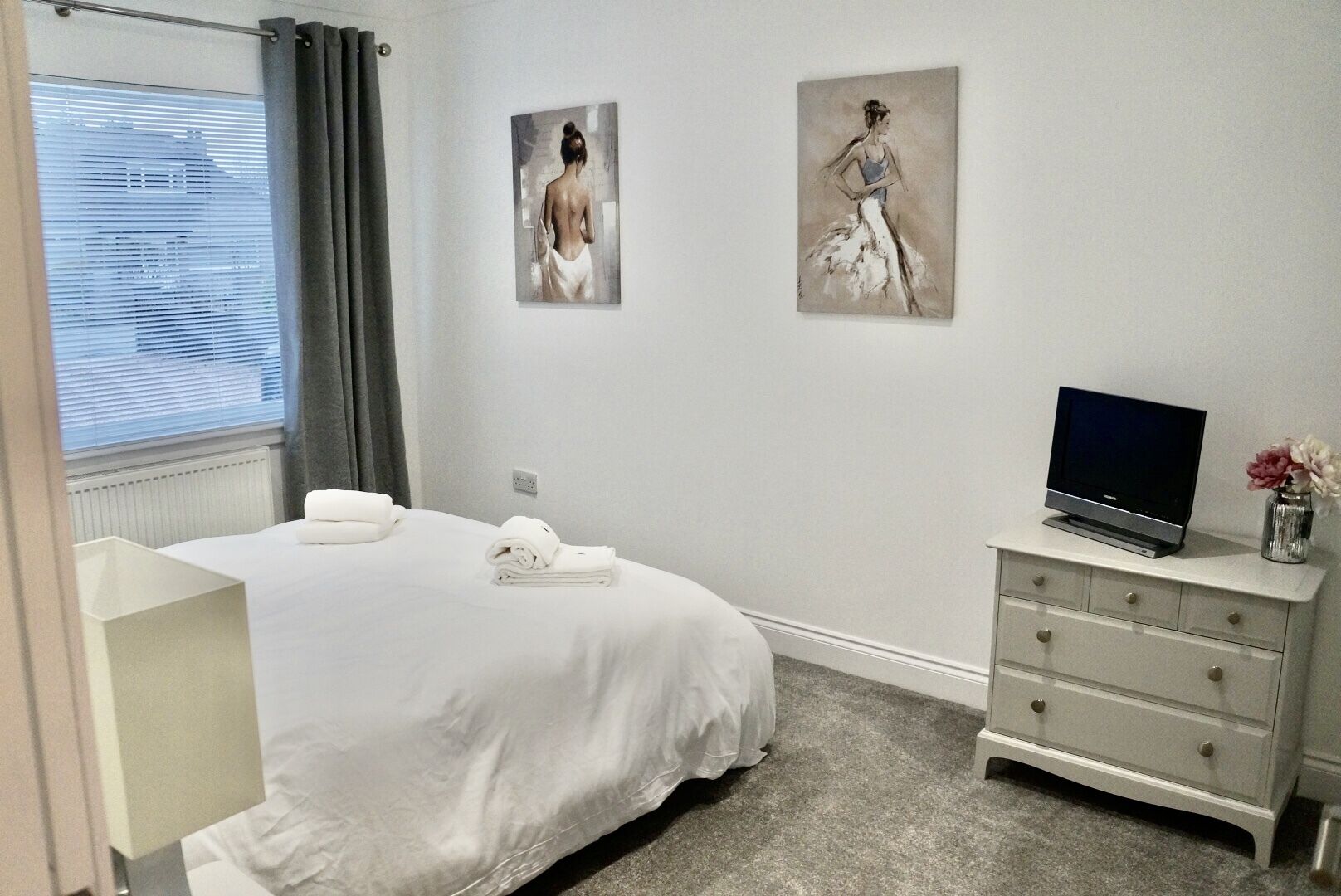 Una habitación de hotel con una cama, un televisor, un aparador y dos cuadros en la pared.