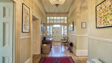 A hallway with a chandelier, framed artwork, and a red patterned rug.