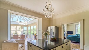 A spacious kitchen with a large island, a chandelier, and a view to a dining area. - Berkeley House (Bath)