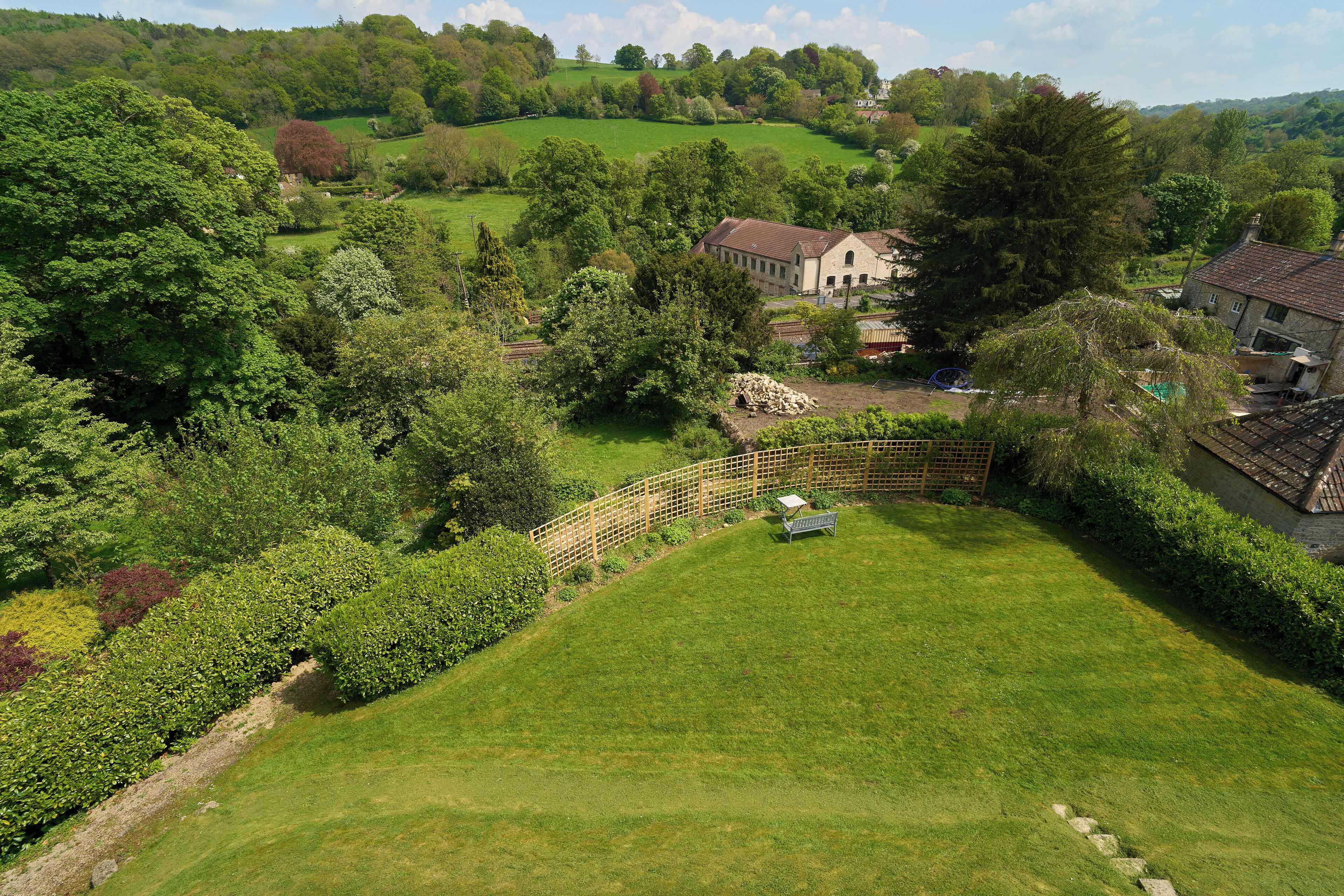 A rural landscape with a large house surrounded by lush greenery and a fenced garden.