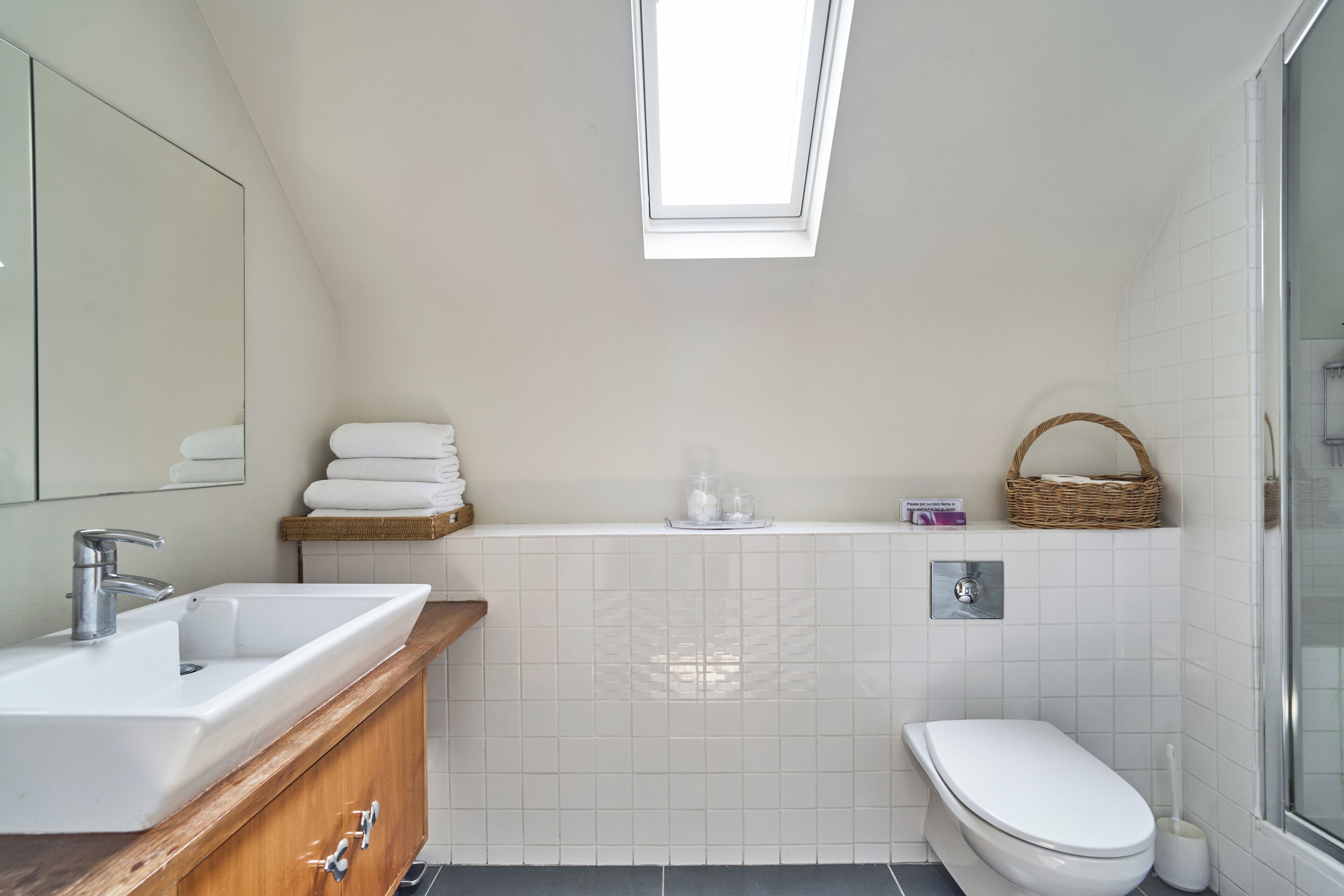 A modern bathroom with a skylight, a sink, a toilet, and a shower area.