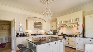 A spacious kitchen with white cabinetry, a central island, and a chandelier. - Berkeley House (Bath)
